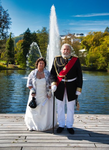Sissi & Ludwig stehen vor dem Kurweiher mit Fontäne im Hintergrund