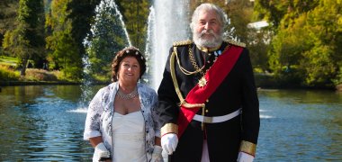 Sissi & Ludwig stehen vor dem Kurweiher mit Fontäne im Hintergrund